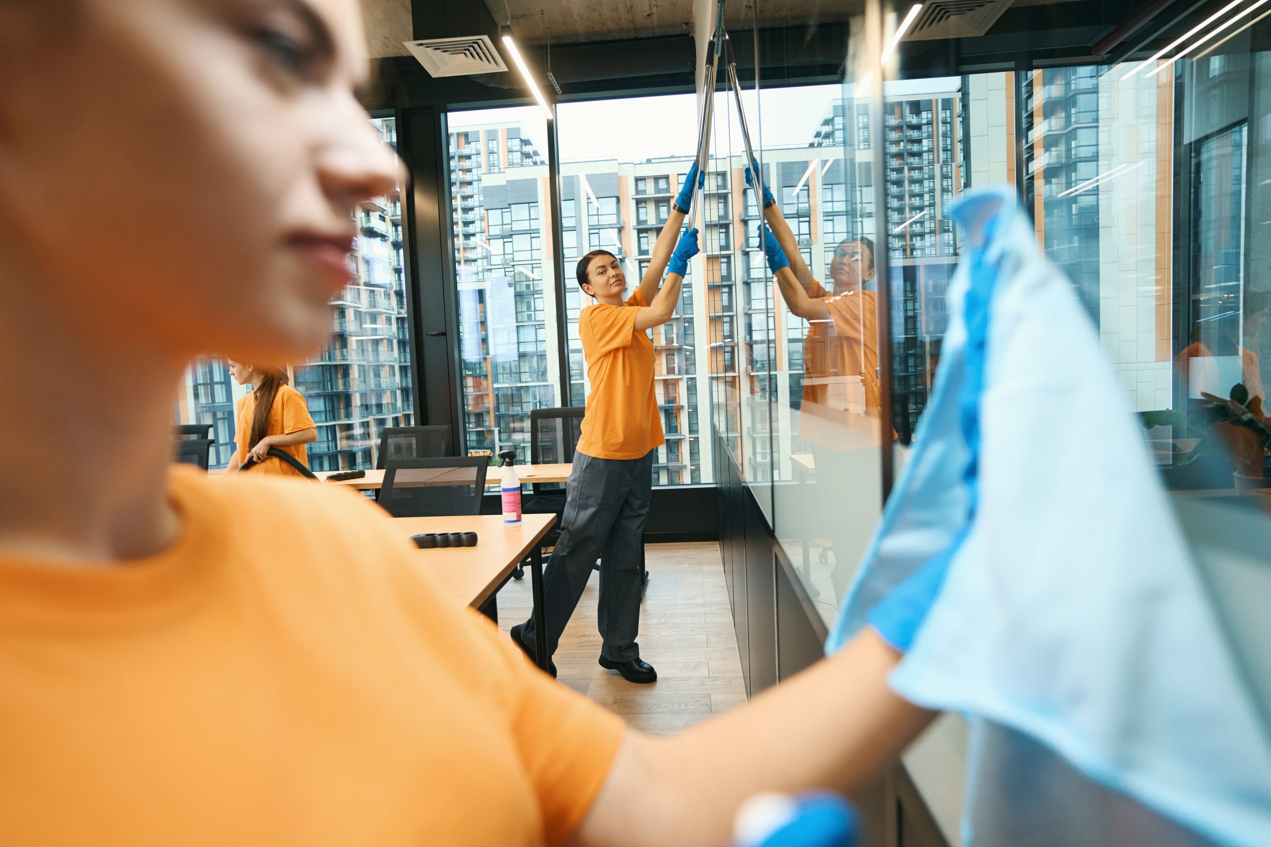 Team of the cleaning company in overalls cleans the coworking space, they use a vacuum cleaner, a mop and napkins